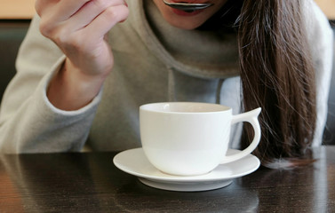 Unrecognizable woman drinks hot tea from cup with a spoon. Close up hands.