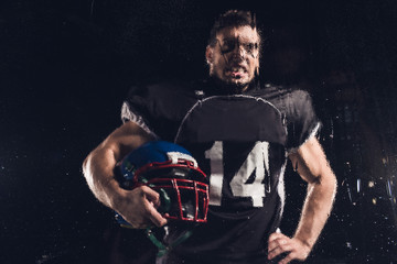 Fototapeta na wymiar view of angry american football player with helmet on black through wet glass