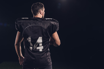 rear view of american football player in black uniform isolated on black