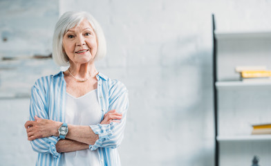 portrait of beautiful smiling senior lady in stylish clothing with arms crossed looking at camera at home