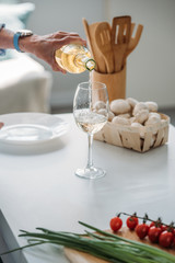 cropped shot of senior woman pouring wine into glass at counter with fresh vegetables in kitchen