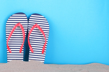 Flip flops in a white and blue strip in the sand on a blue background with a place for an...