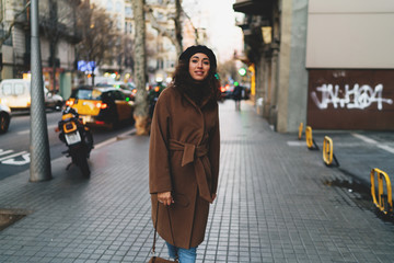 Stylish hipster girl with curly hair enjoying walking the city on a sunny weekend day. Student girl...