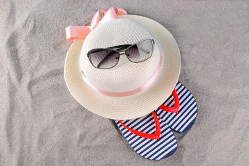 Beach accessories. Hat, flip-flops and sunglasses on the sand of the sea. Top view