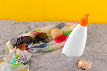 sunscreen with glasses and seashells on the sand on a bright yellow background