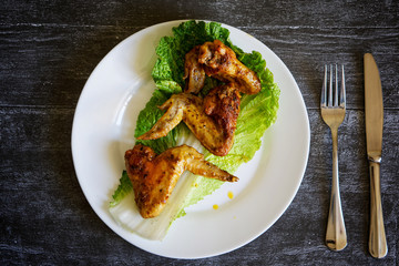 Fried chicken wings in a white plate lie on a dark surface