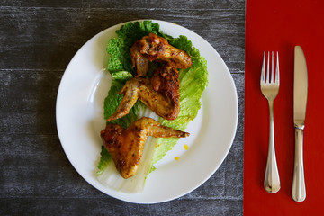 Fried chicken wings in a white plate lie on a black and red surface