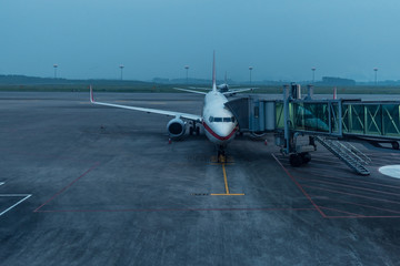 Naklejka na ściany i meble airplane at parking apron view from window of waiting hall of air terminal at dawn on a cloudy day