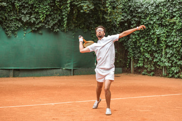 handsome sportsman playing tennis with racket on tennis court