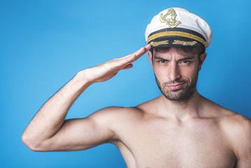 Attractive young sailor making a salutation gesture, blue background, studio image