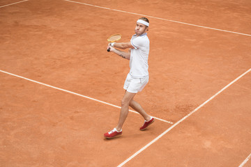 retro styled man in white sportswear playing tennis with wooden racket on court