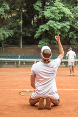 old-fashioned tennis player gesturing up and kneeling after winning match on court