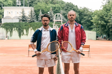 old-fashioned friends with wooden rackets posing on tennis court with net