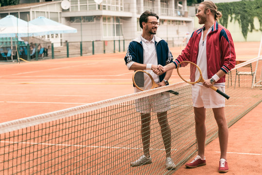 friends with wooden rackets shaking hands on tennis court with net
