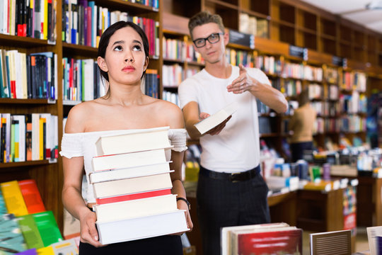 Young man giving book to tired sad girl with stack of books in h
