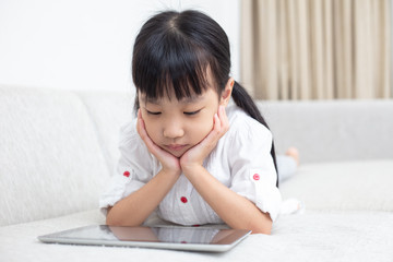 Asian Chinese little girl lying on the sofa and playing tablet