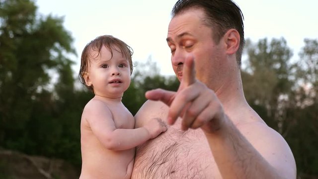 Small wet bathing child laughs, sitting in arms of happy father.