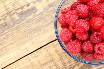 Close up of ripe raspberries in the glass bowl on wooden boards