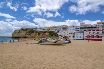 Playa de arena con barcas entre acantilados y en frente de la encantadora arquitectura blanca en Carvoeiro, Algarve, Portugal