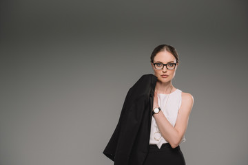 portrait of businesswoman in eyeglasses holding jacket isolated on grey background