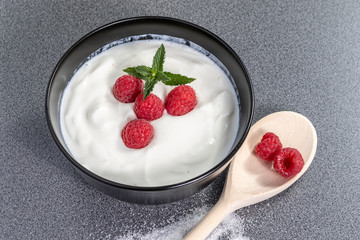 Black bowl full of curd and ripe raspberries on top decorated with a green mint leaf