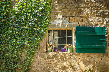 Fototapeta na wymiar An ancient window with green shutters on the stone wall of the house.