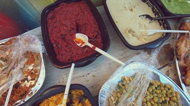 Traveling Shot Over A Colourful Food Buffet With Plastic Containers, Plastic Cling Wrap And Cutlery, Leaching Harmful Chemicals Into The Party Food. A Female Hand Is Choosing A Chicken Wing.