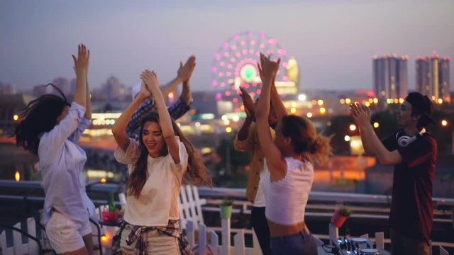 Slow motion of young people dancing and clapping hands at hight rooftop party with professional deejay. Men and women are having fun and relaxing at weekend.