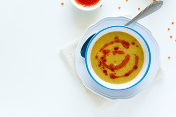 Red lentil soup with chili pepper sauce and bread on white wooden table