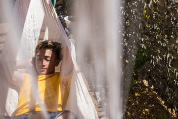 beautiful caucasian young boy stay and rest on an hammock outdoor in the nature. serious expression...