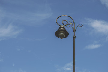 Klasyczna latarnia uliczna na tle błękitnego nieba z małymi, białymi chmurami - obrazy, fototapety, plakaty