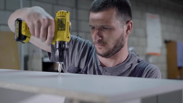 Worker man using drill for wooden panel in factory white