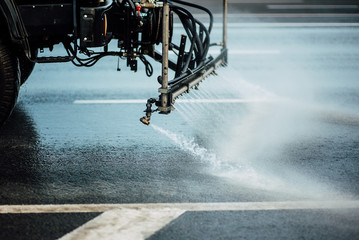 Cleaning sweeper machines washes the city asphalt road with water spray.
