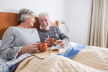 nice caucasian aged senior couple enjoying and laughing together waking up in the early morning. toasted and marmelade and coffee. togetherness and foreverness concept. people smiling and loving - obrazy, fototapety, plakaty