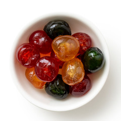 Red, green and yellow glace cherries in white bowl isolated on white from above.