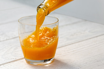 Pouring orange juice from a glass bottle into a glass. White wood background.