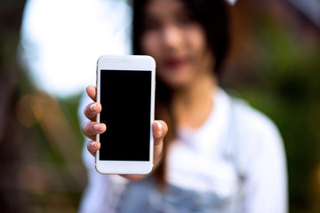 Mockup image of a woman holding and displaying a white mobile phone with a black screen with a blank screen on a table in a modern cafe. Ideas for working with communication tools.