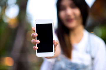 Mockup image of a woman holding and displaying a white mobile phone with a black screen with a blank screen on a table in a modern cafe. Ideas for working with communication tools.