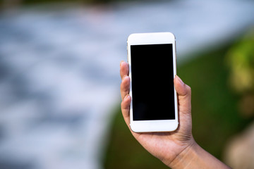 Mockup image of a woman holding and displaying a white mobile phone with a black screen with a blank screen on a table in a modern cafe. Ideas for working with communication tools.