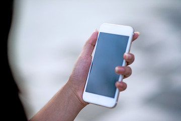 Mockup image of a woman holding and displaying a white mobile phone with a black screen with a blank screen on a table in a modern cafe. Ideas for working with communication tools.