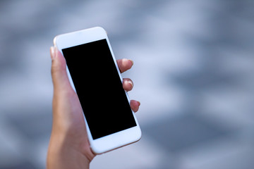Mockup image of a woman holding and displaying a white mobile phone with a black screen with a blank screen on a table in a modern cafe. Ideas for working with communication tools.