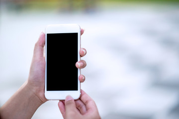 Mockup image of a woman holding and displaying a white mobile phone with a black screen with a blank screen on a table in a modern cafe. Ideas for working with communication tools.
