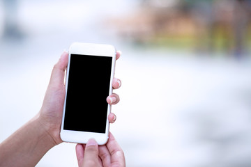 Mockup image of a woman holding and displaying a white mobile phone with a black screen with a blank screen on a table in a modern cafe. Ideas for working with communication tools.