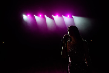 Girl in long gown performing on stage. Girl singing on the stage in front of the lights. Silhouette...