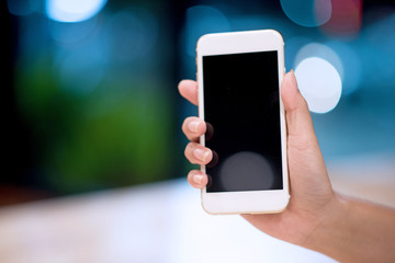 Mockup image of a woman holding and displaying a white mobile phone with a black screen with a blank screen on a table in a modern cafe. Ideas for working with communication tools.