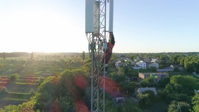 drone view of cellular antenna, radio telecommunication tower with worker on background of beautiful city landscape in sunlight