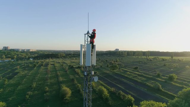 engineer with a gadget connected a mobile communication on radio telecommunication tower on background of blue sky with sunset