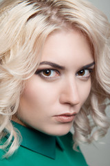 Blond girl with hair and makeup in green dress on gray isolated background close-up.