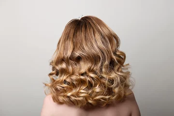 Printed roller blinds Hairdressers Female hairstyle with long curls on the head of a blonde with a back view on a gray background.