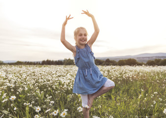 child on green daisy grass in a summer park sunset time doing balerina © Louis-Paul Photo